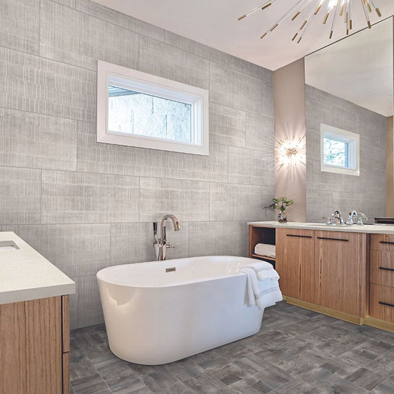 Bathroom with seasoned wood look floor tile, gray fabric look wall tile, soaker tub, separate natural wood vanities with white quartz counters, starburst lighting.