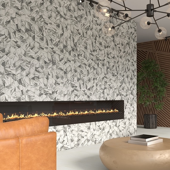 Hotel lounge area with white and gray marble mosaic wall with long electric fireplace, light beige floor tile, terracotta leather chair, and large round coffee table.