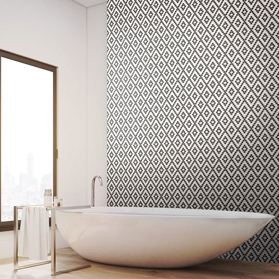 White, long soaker bathtub in front of a large picture window and black & white mosaic feature wall, and floor tile that looks like wood.