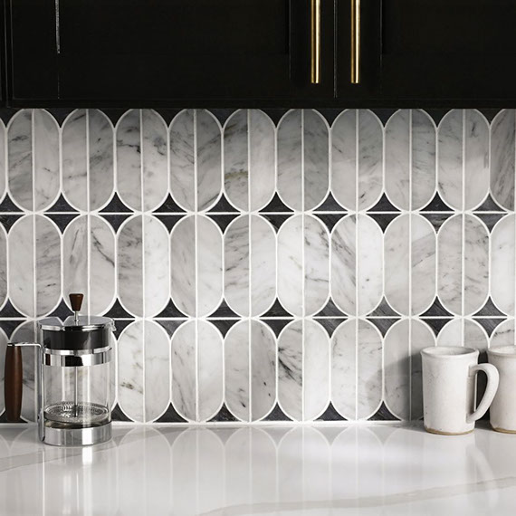 Closeup of kitchen backsplash of pre-cut gray & white marble mosaic with black marble accents, white quartz countertop, French press, coffee mugs.