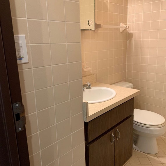 Before photo of half bath with square beige wall tile, dark wood vanity with beige Formica countertop, mirrored medicine cabinet over sink.